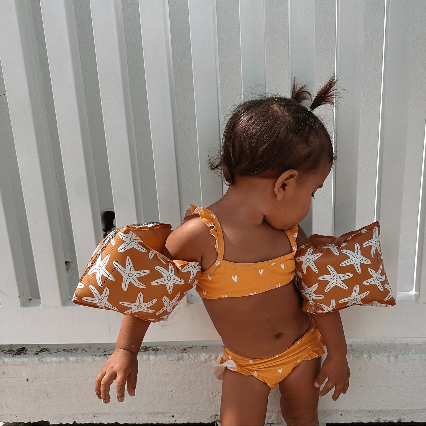 Bambina con braccioli stelle marine in piscina