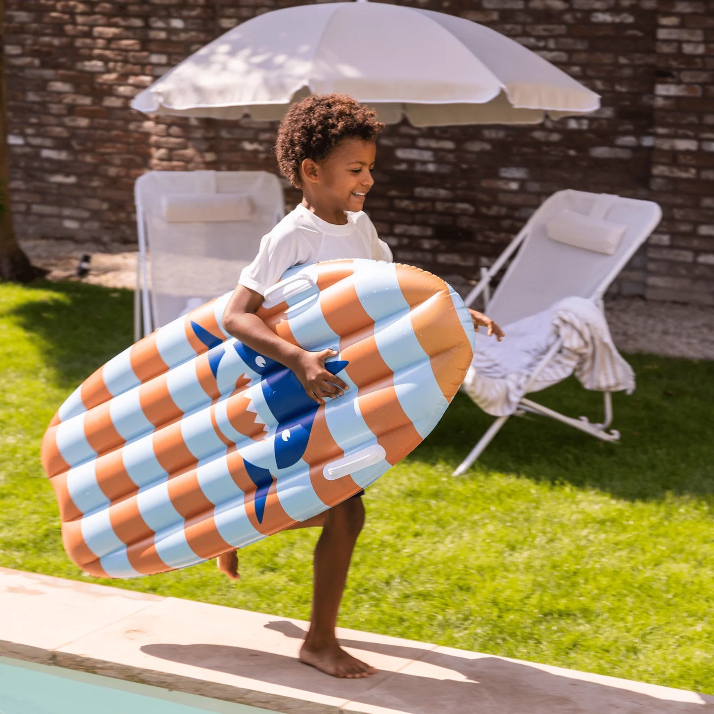 Bambino con surfboard Stride Shark in giardino vicino alla piscina