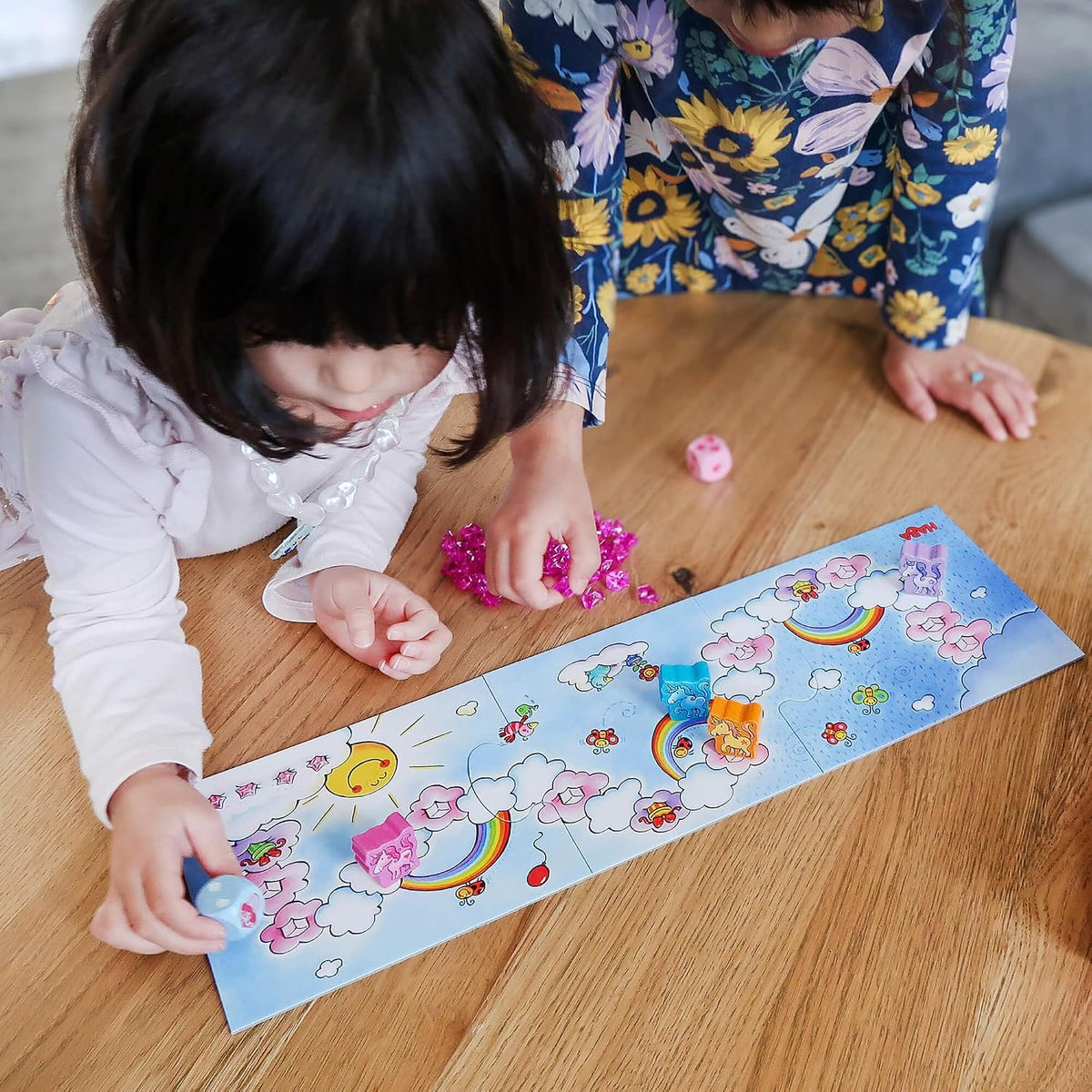 Due bambini giocano a Liocorno Luccichino Haba, con pedine unicorno sul tabellone, dadi e cristalli rosa