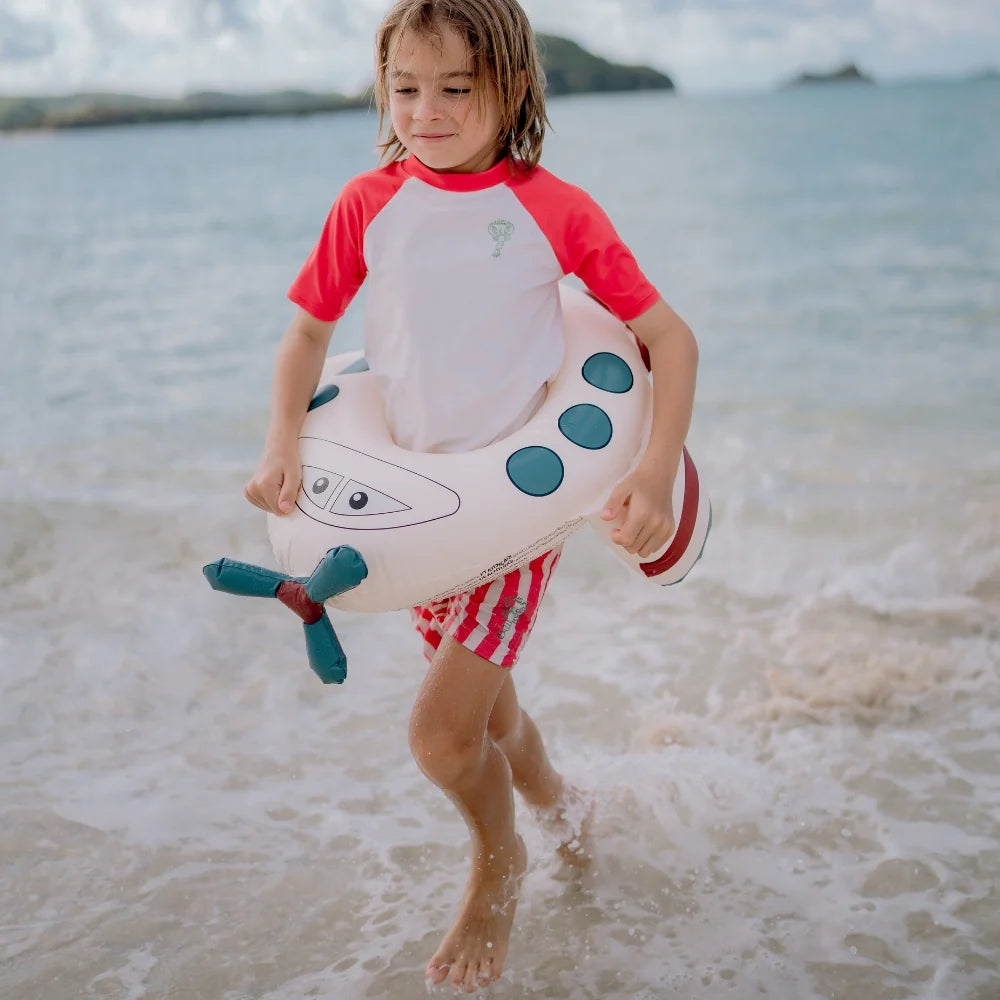Bambino in spiaggia con ciambella Peter Plane Swim Essentials tra le onde